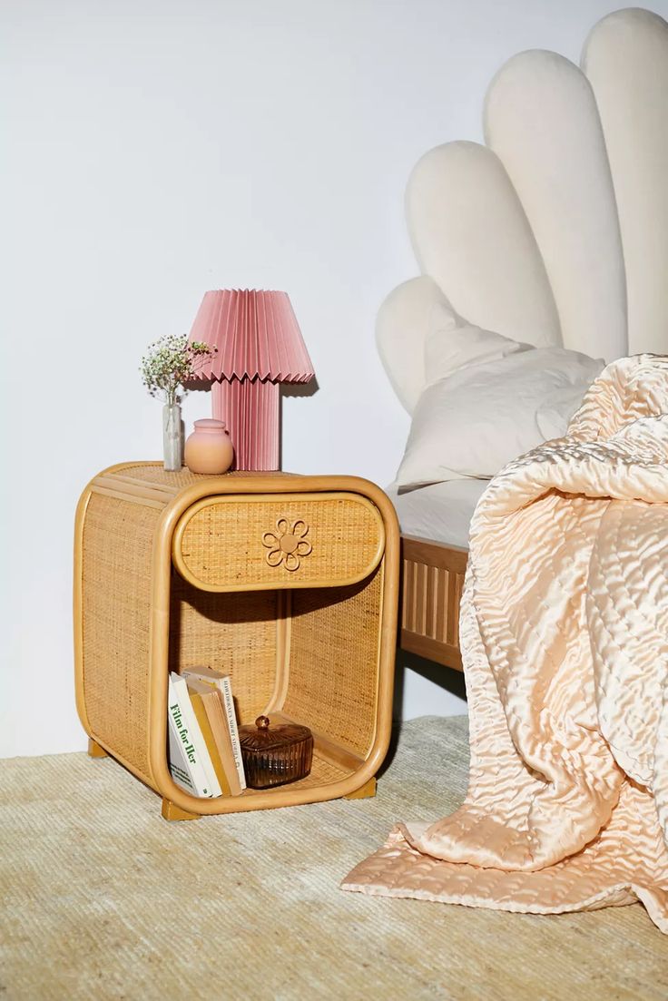 a small wooden table with a lamp on it next to a bed and a blanket