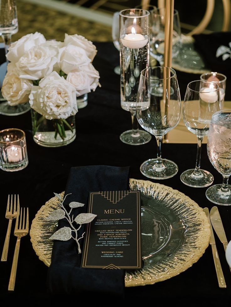 a black table with white flowers and silverware on it is set for a formal dinner