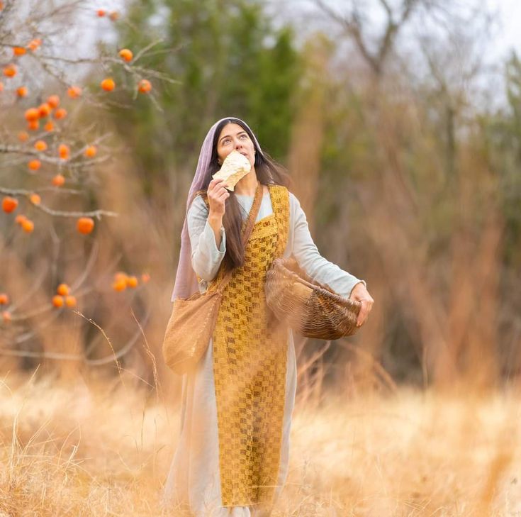 a woman standing in a field with an orange and white scarf on her head eating something