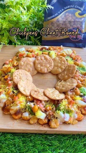 a wooden cutting board topped with crackers and veggies next to a bag of chips