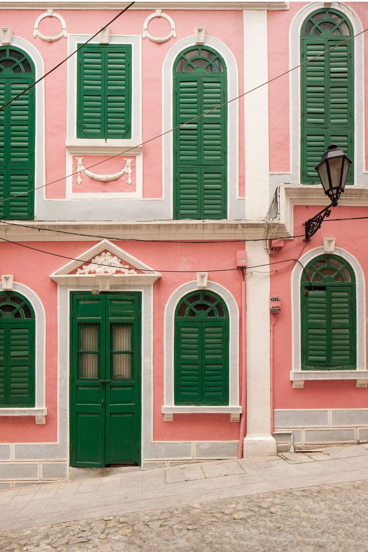 an old pink building with green shutters and a street light in front of it