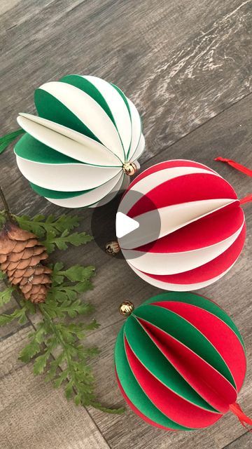 three paper christmas ornaments sitting on top of a wooden table next to a pine cone