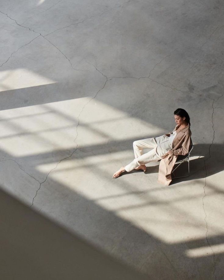 a woman sitting on top of a white chair next to a window in an empty room