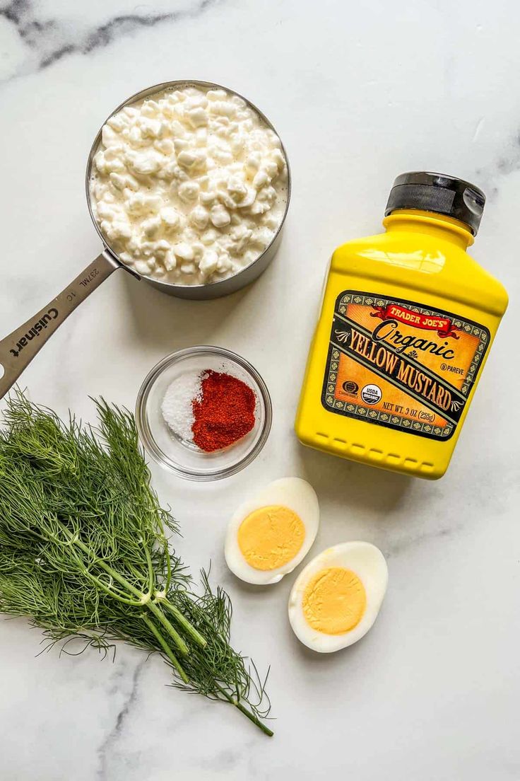 ingredients to make deviled eggs laid out on a marble counter top, including yogurt and dill