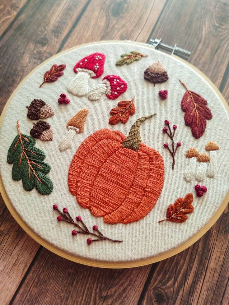 an embroidered pumpkin surrounded by autumn leaves and acorns on a wooden table top