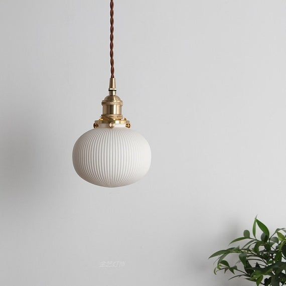 a white lamp hanging from a ceiling next to a potted plant on a table