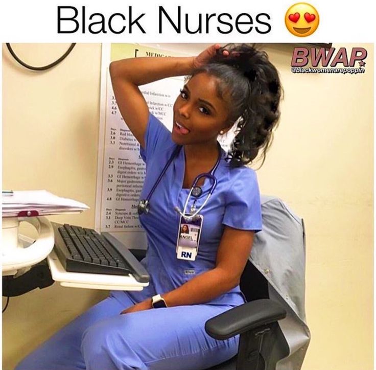 a woman in scrubs sitting at a desk with a computer and monitor on the wall