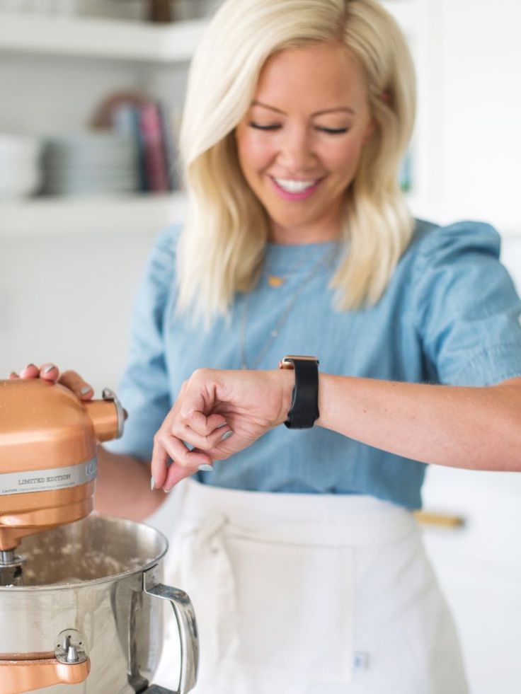 a woman standing in front of a mixer smiling at the camera while holding her hand on the handle