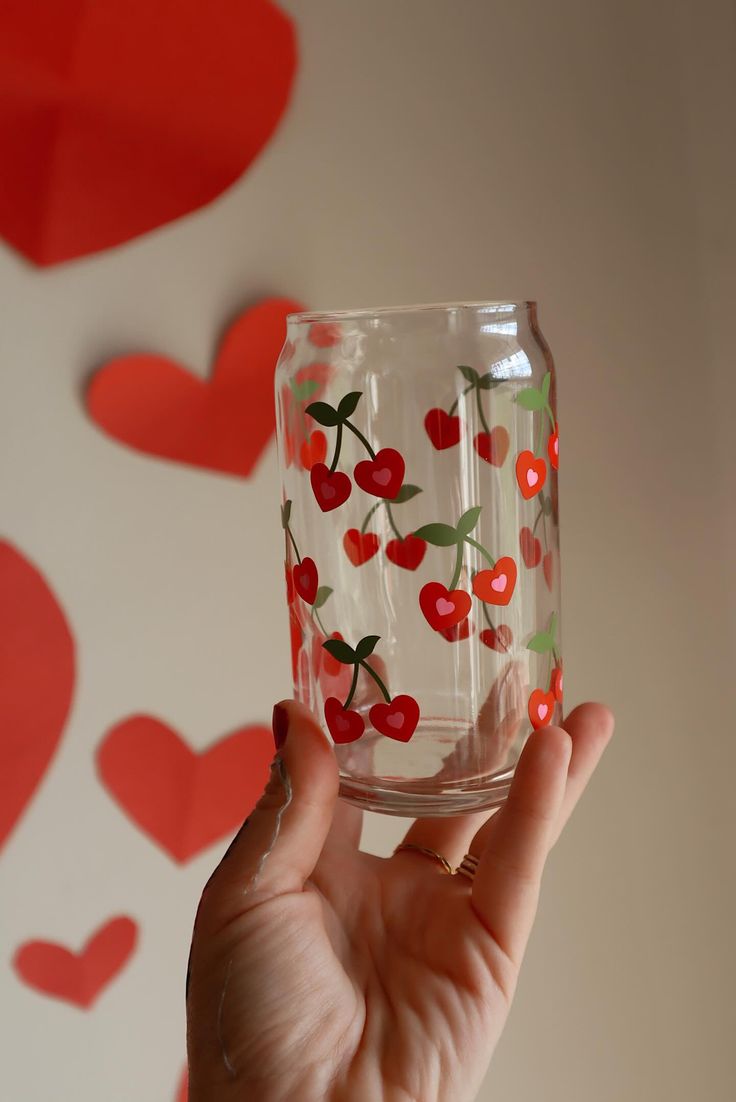 a hand holding up a glass with cherries on it and hearts in the background