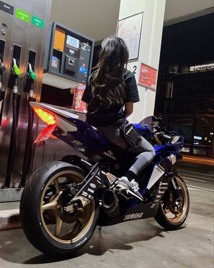 a woman sitting on a motorcycle at a gas pump