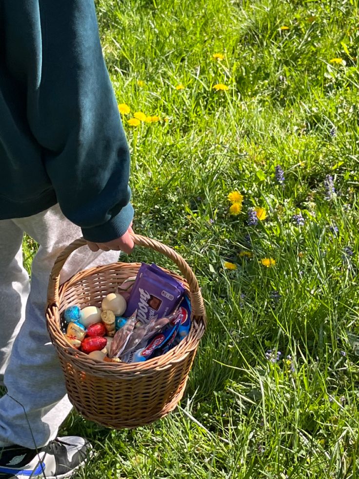 a person holding a basket full of candy and candies in the grass with dandelions