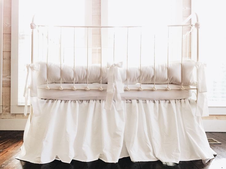 a white crib with black ruffled bedding in front of a window and wooden floor