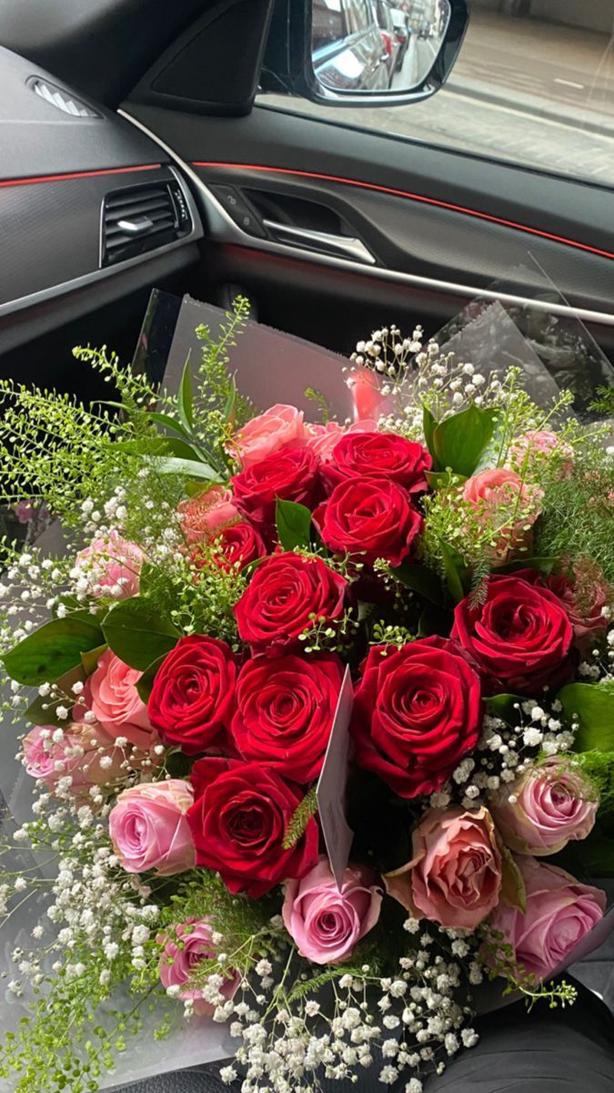 a bouquet of red and pink roses sitting on the dashboard of a car