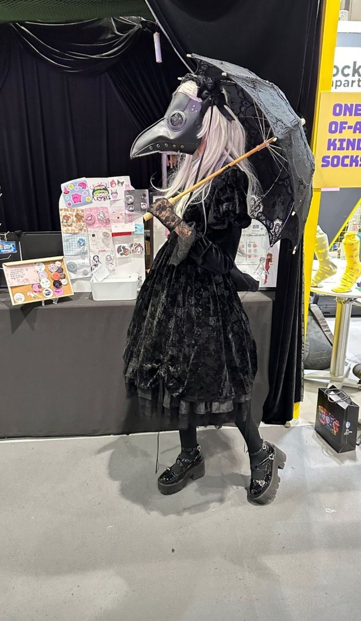 a woman dressed in black holding an umbrella and standing next to a table with pictures on it