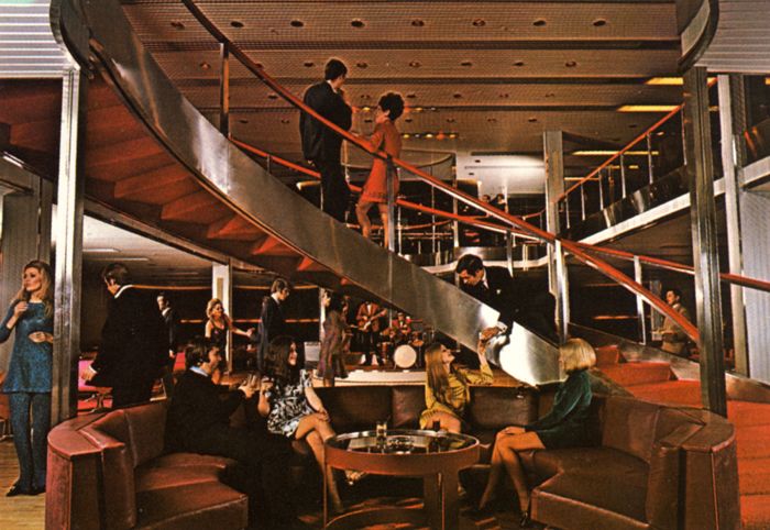 several people are gathered in a lobby with metal railings and escalators on the second floor