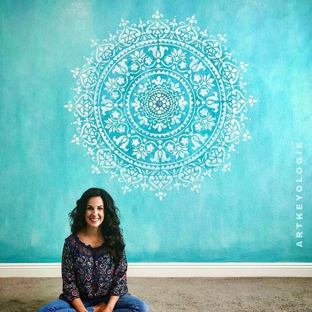 a woman sitting on the floor in front of a wall with a blue and white design