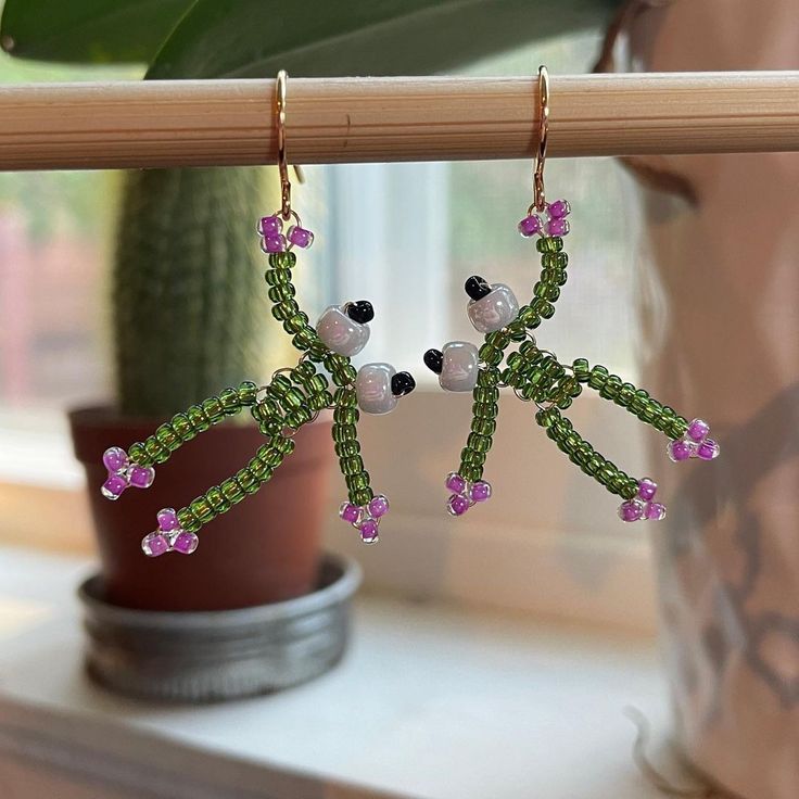 the earrings are decorated with beads and pink flowers on green stems in front of a potted plant