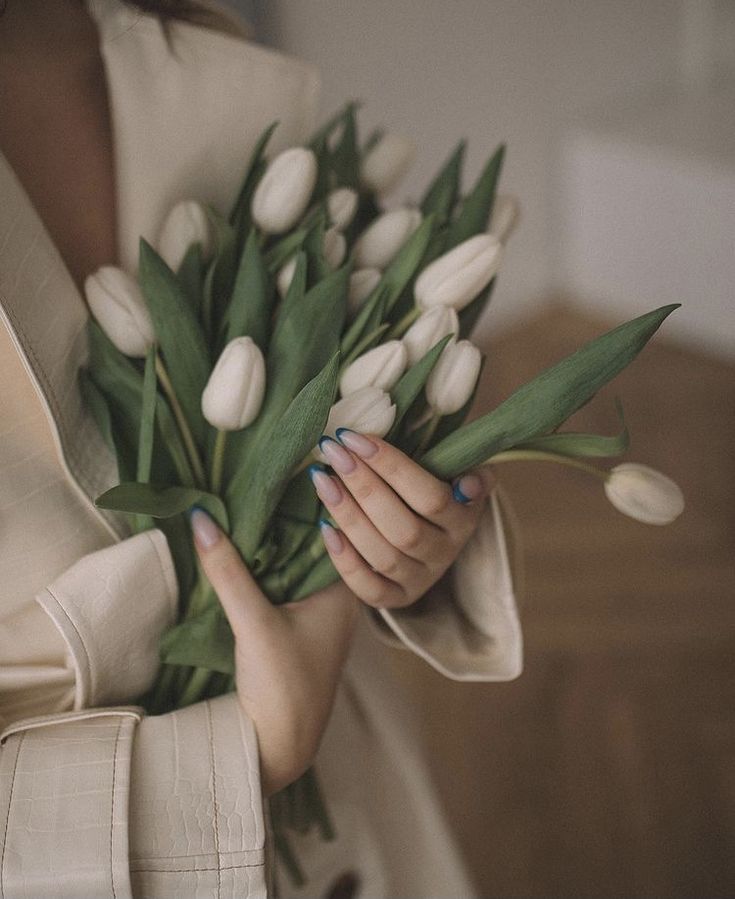 a woman holding a bouquet of white tulips with green leaves in her hands