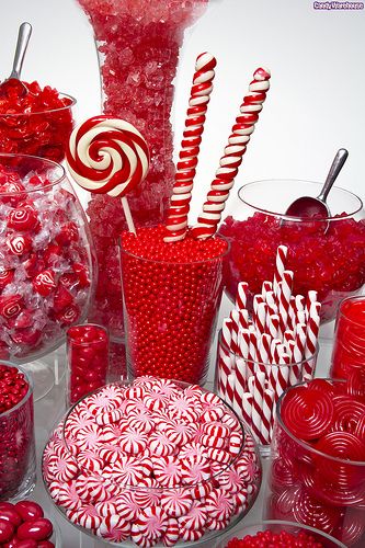 a table topped with lots of red and white candies next to large glass vases filled with candy