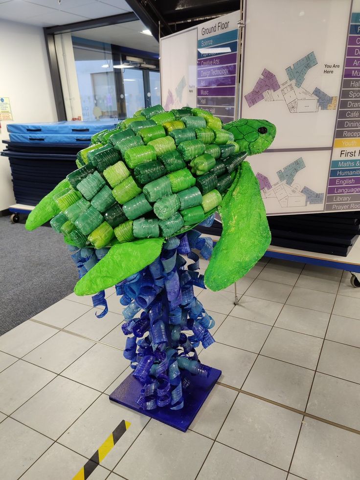 there is a sculpture made out of green and blue plastic bottles in the middle of a tiled floor