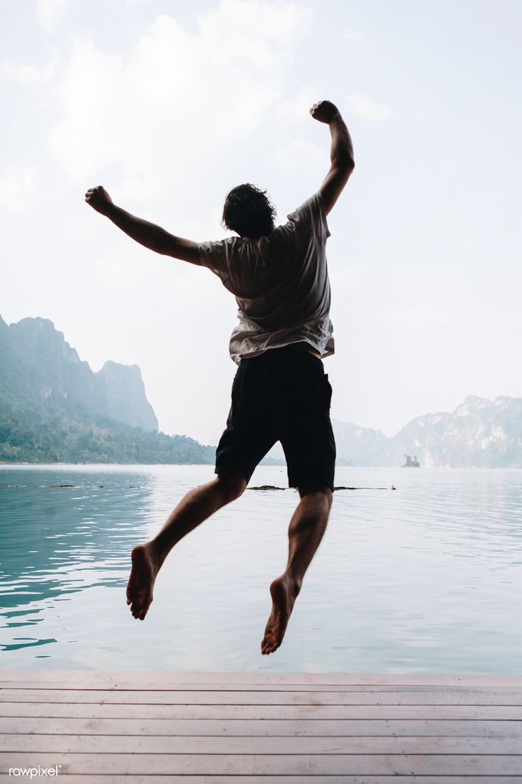 a man is jumping into the water from a dock with his arms in the air