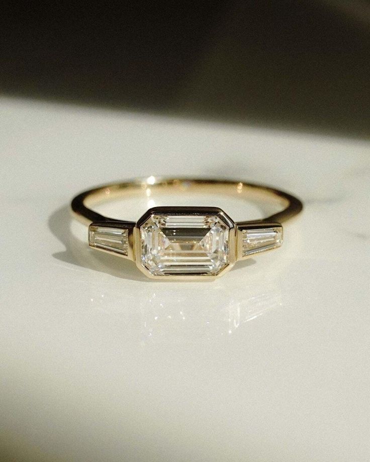 an engagement ring with three baguets on it, sitting on a white surface