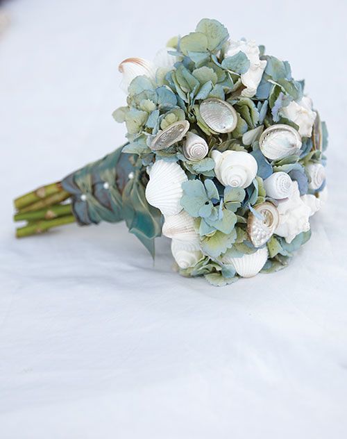 a bridal bouquet with seashells and greenery sits on a white surface