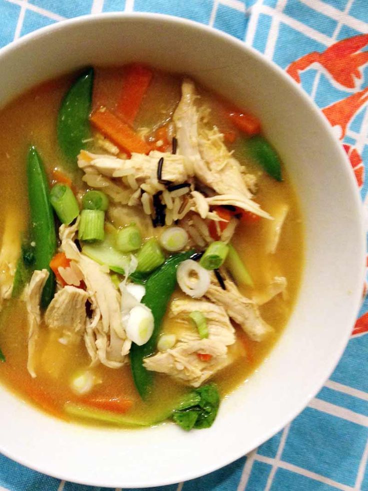 a white bowl filled with chicken and veggies on top of a blue table cloth