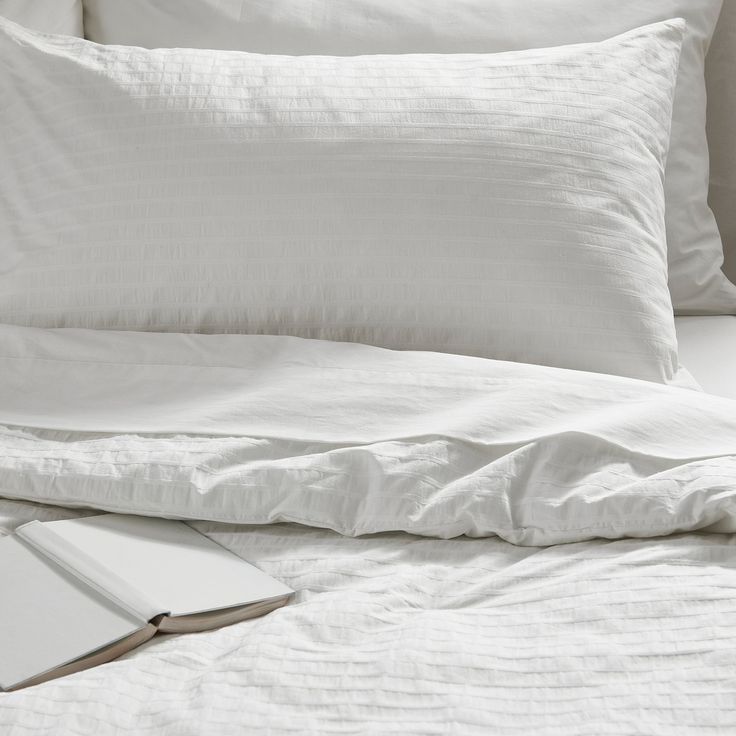 an open book on a bed with white linens and pillows in the foreground