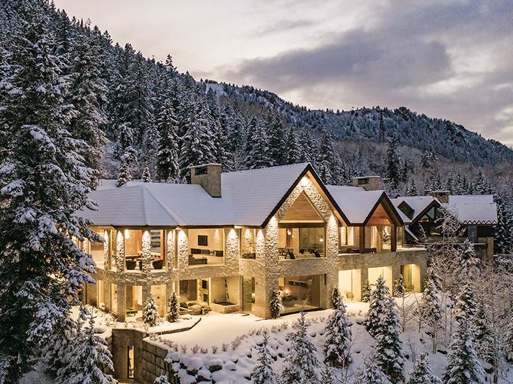 a large house surrounded by trees covered in snow at night with lights on the windows