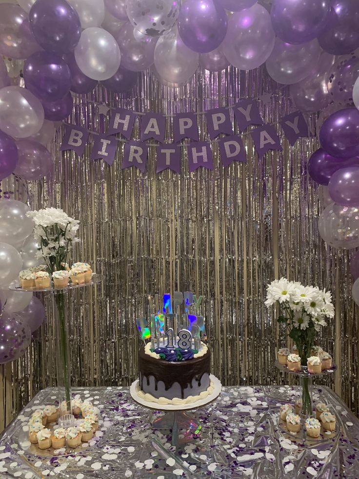 a birthday cake and cupcakes sitting on a table with balloons in the background