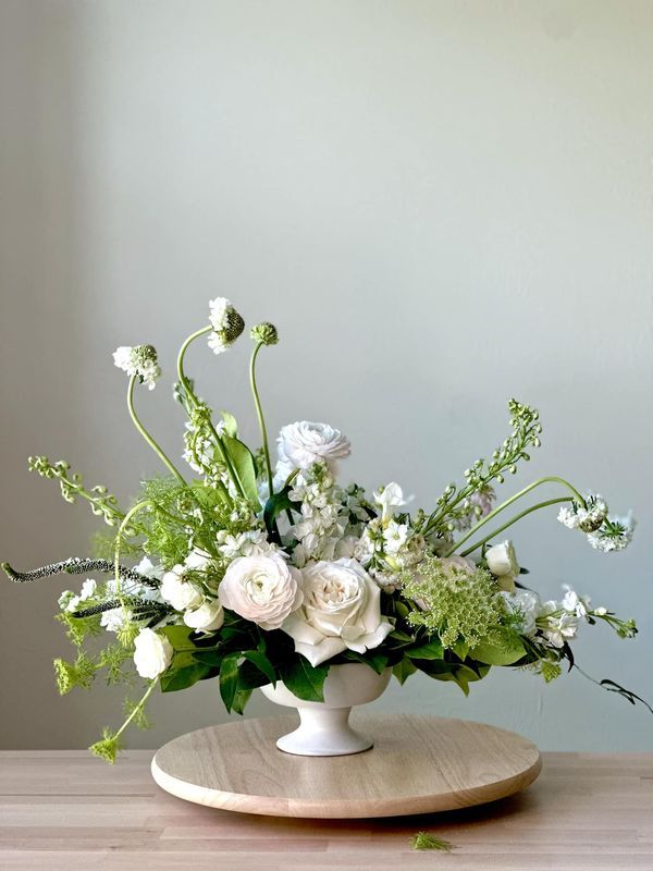 a white flower arrangement sitting on top of a wooden table