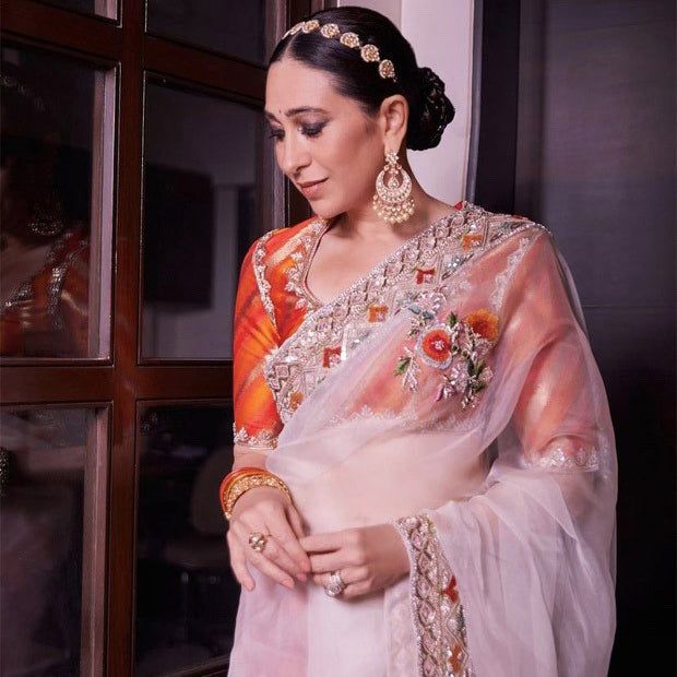 a woman in an orange and white sari is looking down at her hand on her hip