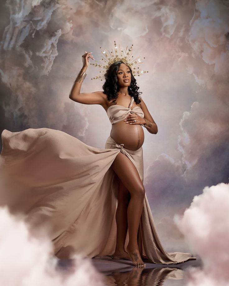 a pregnant woman wearing a dress and crown standing in the clouds with her hands up