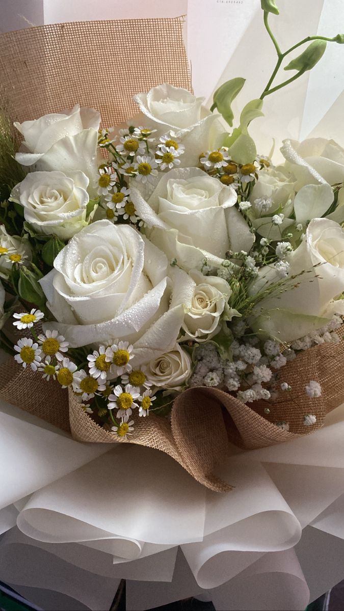 a bouquet of white roses and daisies in burlock