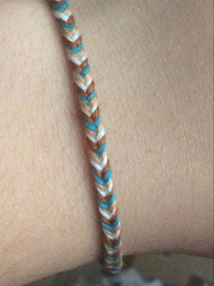 a close up of a person's arm with a bracelet on it that has an orange and white braid