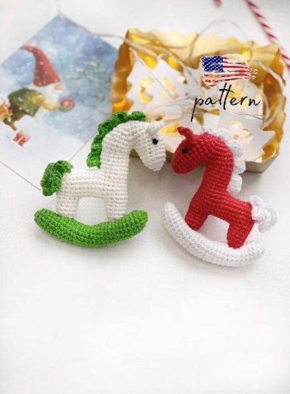 two crocheted horses are sitting next to each other on a table with christmas decorations in the background