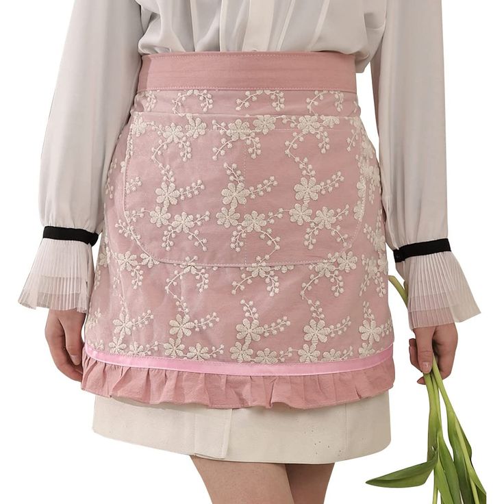 a woman holding a flower in her right hand and wearing a pink skirt with white flowers on it