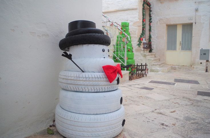 a snowman made out of old tires sitting on the side of a building with a red bow