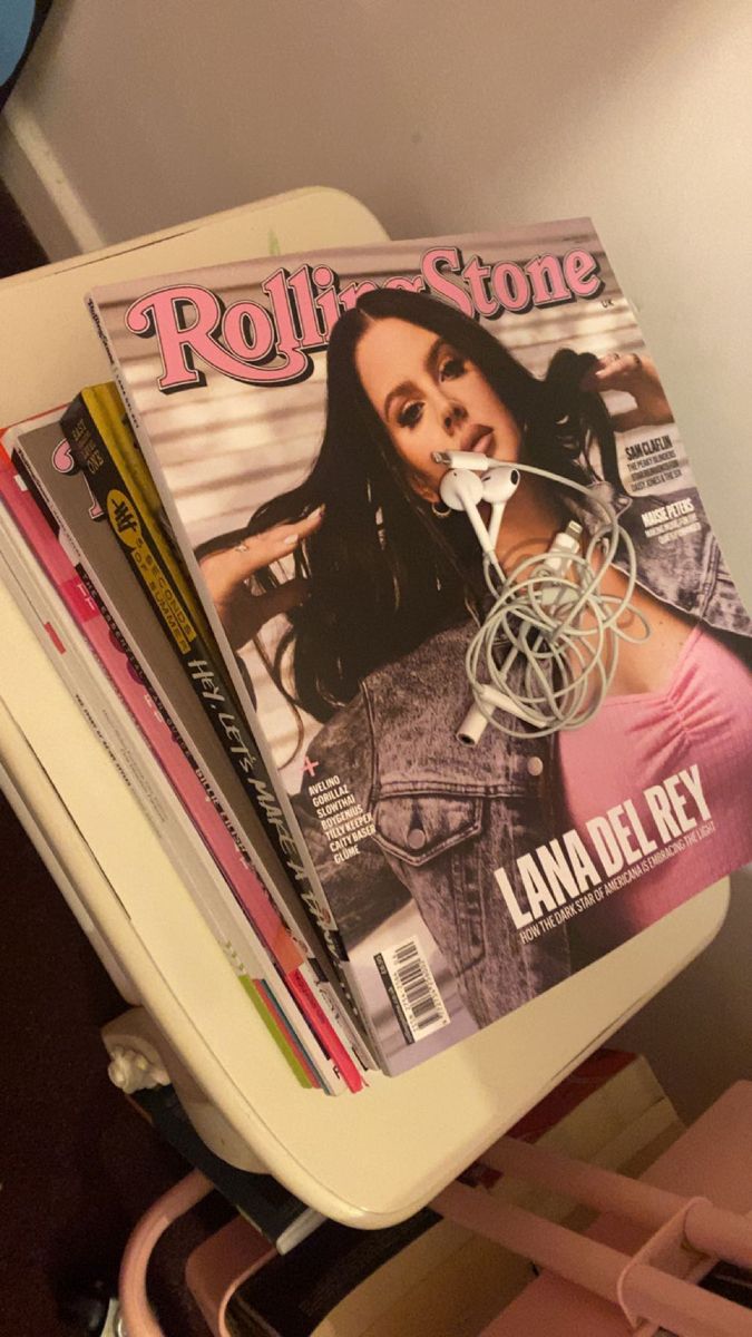 magazines stacked on top of each other in front of a white shelf with pink chairs