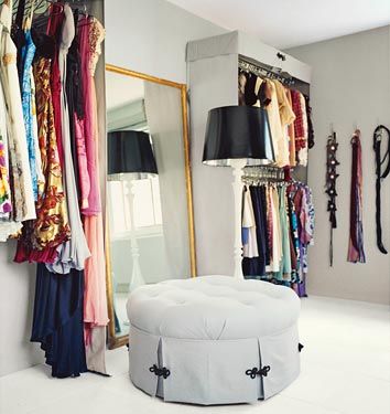 a room with clothes hanging on the wall and a round ottoman in front of a mirror