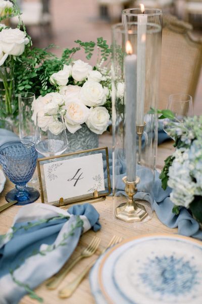 the table is set with blue and white plates, silverware, flowers and candles