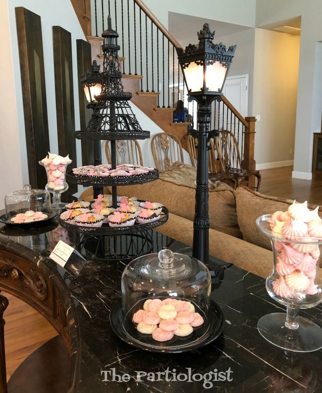 a table topped with cakes and cupcakes under a chandelier next to a stair case