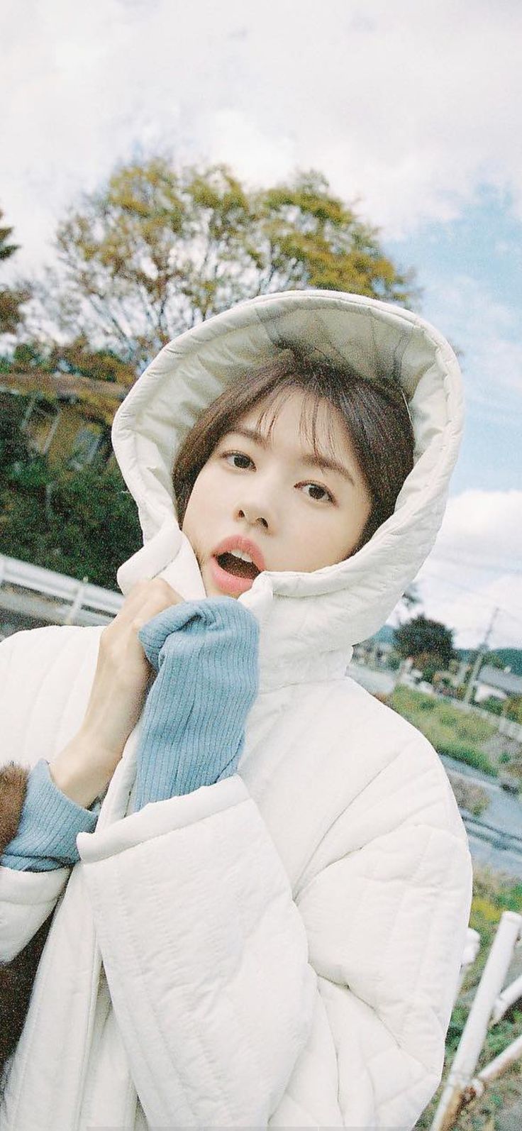 a woman in a white jacket and blue mittens is posing for the camera with her hand on her shoulder