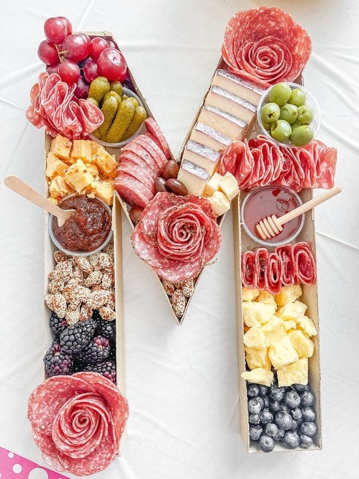 an assortment of meats, cheeses and fruit arranged in the shape of the letter m