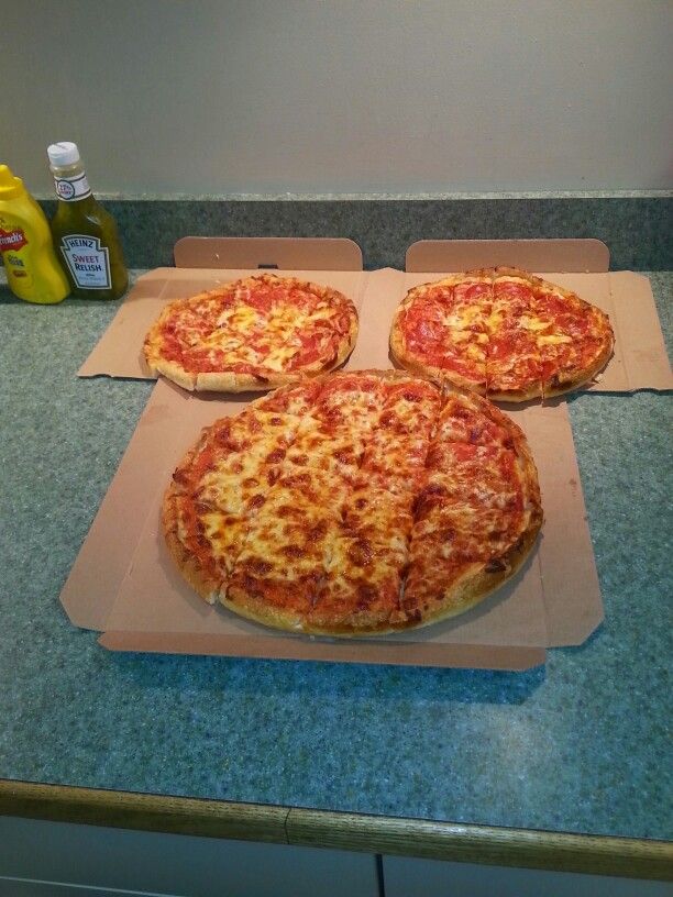 three pizzas sitting on top of a counter next to bottles of mustard and ketchup