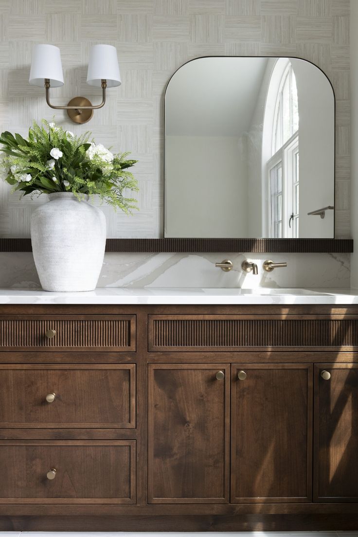 a bathroom sink with a large mirror above it and flowers in a vase on the counter