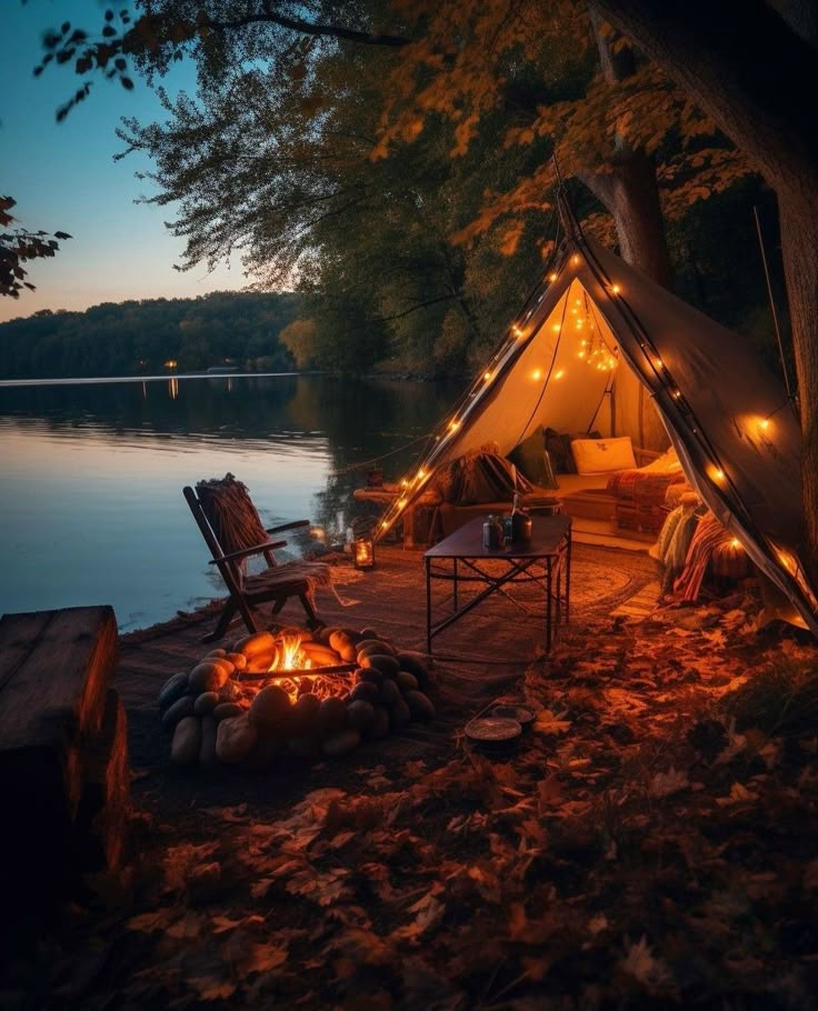 a tent is lit up with fairy lights and chairs around the campfire at night