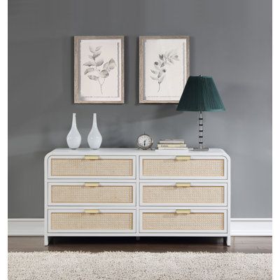 a white dresser with two paintings on the wall above it and a lamp next to it