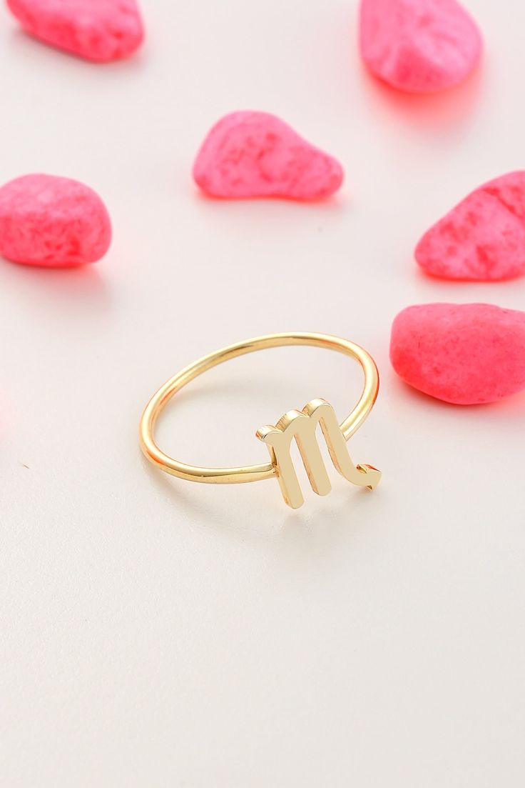 a gold ring with the letter y on it surrounded by small pink rocks and pebbles